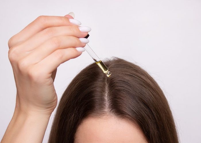 A person applying a dropper on her head Description automatically generated